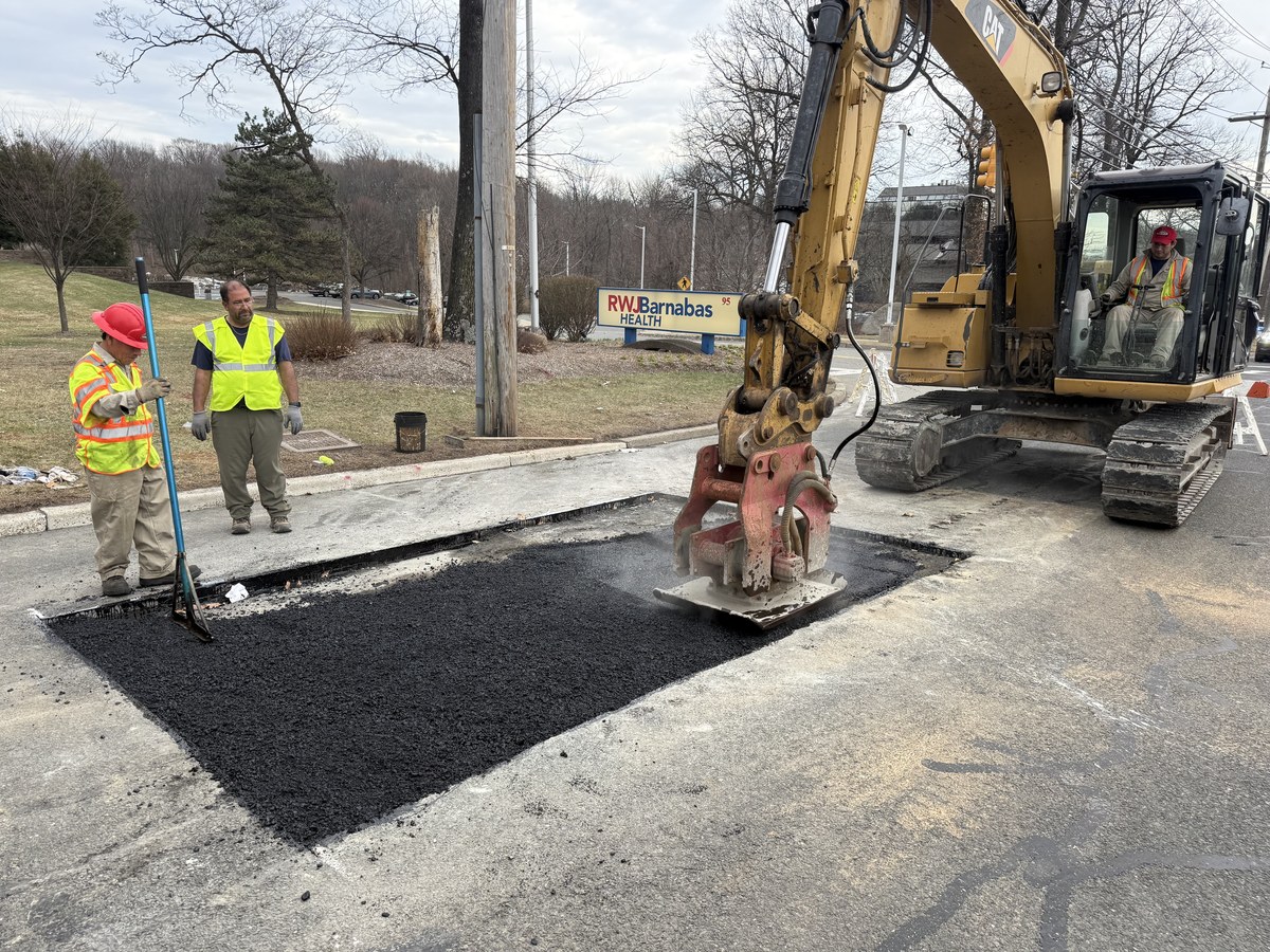 Crew finishing an asphalt patch / pothole repair with a CAT 352 excavator and compactor.
