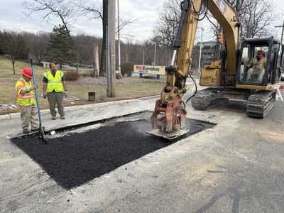 Crew finishing an asphalt patch / pothole repair with a CAT 352 excavator and compactor.