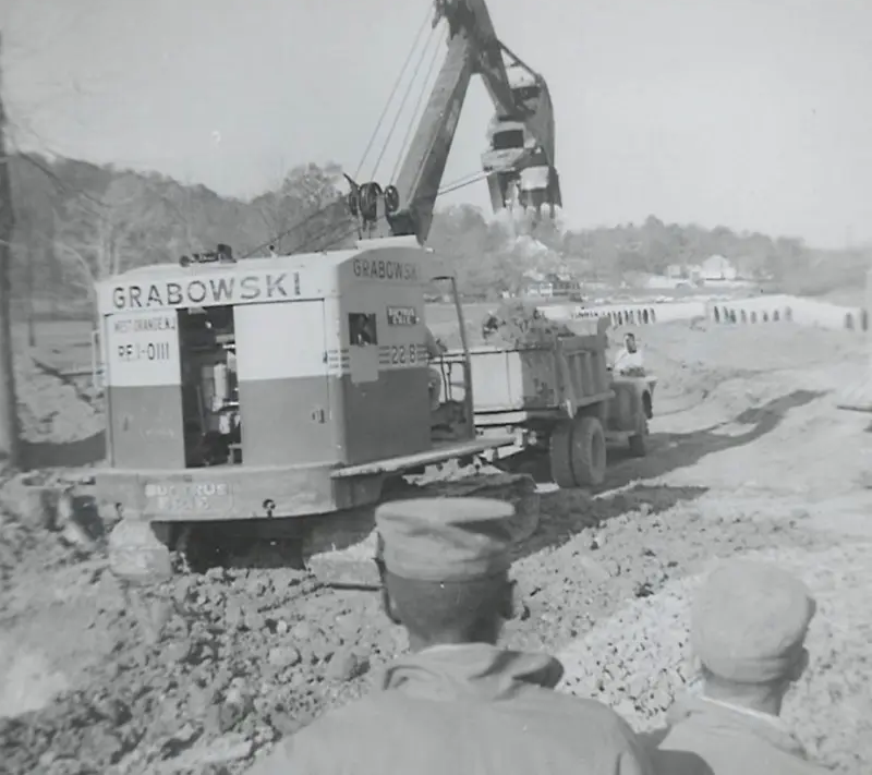 B&W vintage GRABOWSKI shovel rig with dump trucks at a quarry.