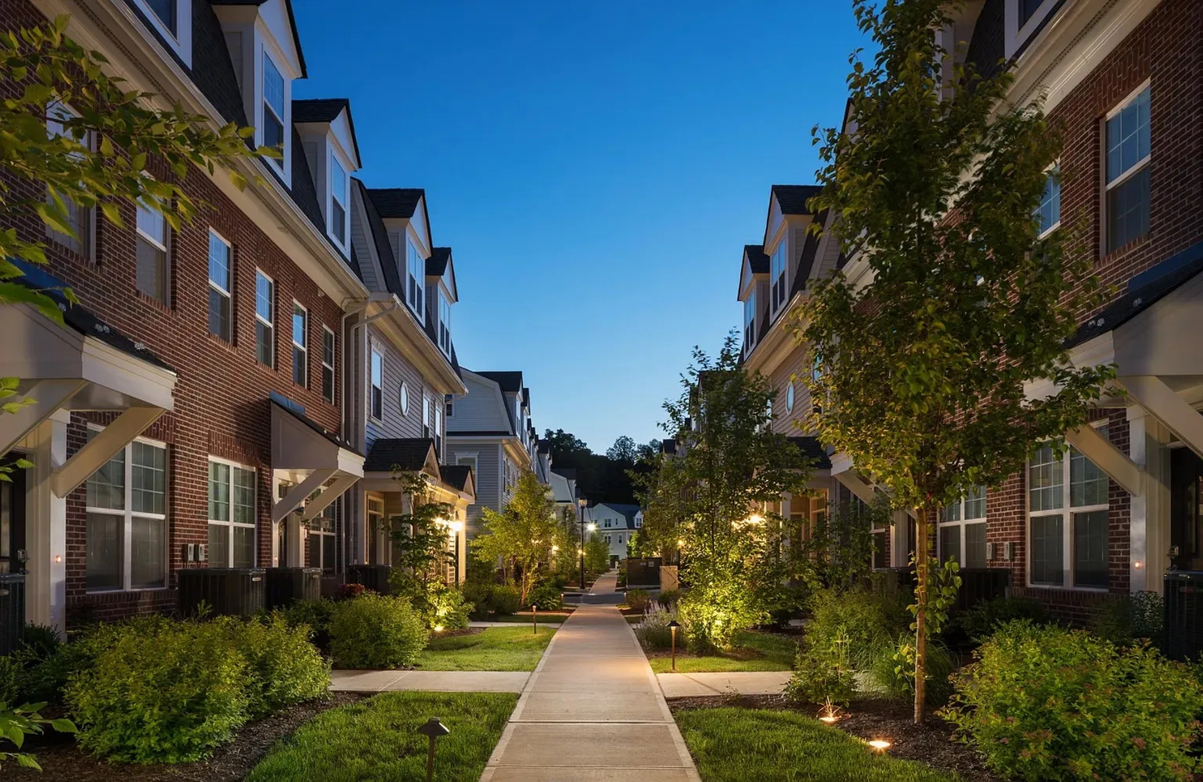 Estling Village — completed townhomes with paved pathway between rows, landscape lighting at dusk.