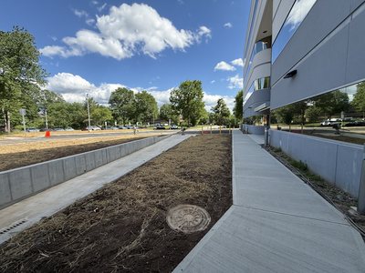 Concrete walkway and loading-dock wall running along the curved glass facade of the Marotta Controls building.