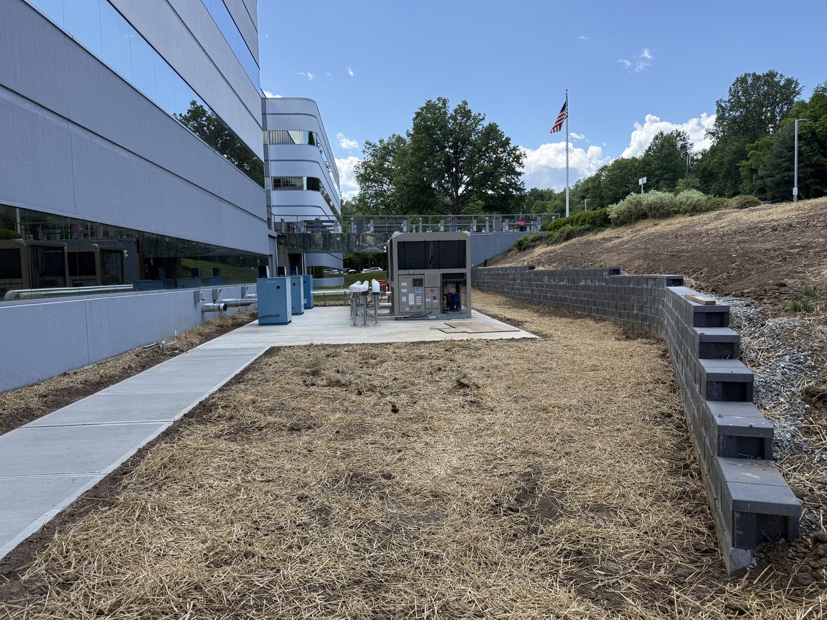 Tiered segmental block retaining wall and new concrete walkway beside the equipment pad at Marotta Controls.