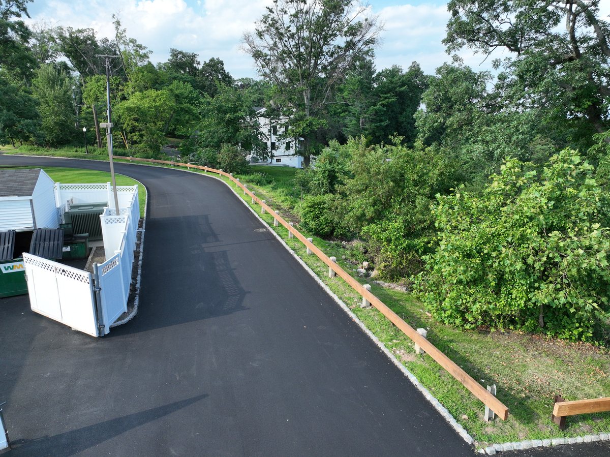 New timber guardrail on concrete posts along the freshly paved hillside drive.