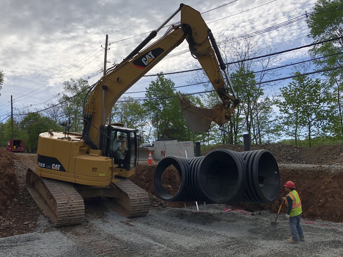 CAT excavator setting large-diameter HDPE drainage pipe in the trench during site development for the temple.