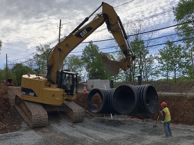 CAT excavator setting large-diameter HDPE drainage pipe in the trench during site development for the temple.