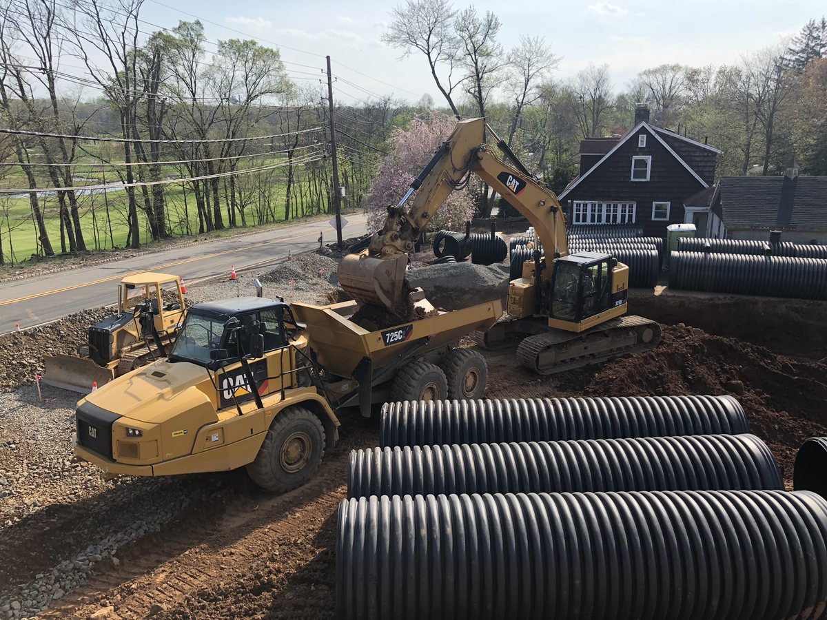 CAT articulated dump truck and excavator working beside staged HDPE drainage pipe on the temple site.