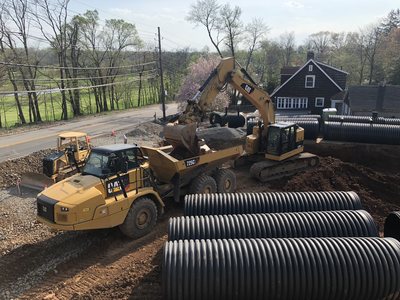 CAT articulated dump truck and excavator working beside staged HDPE drainage pipe on the temple site.