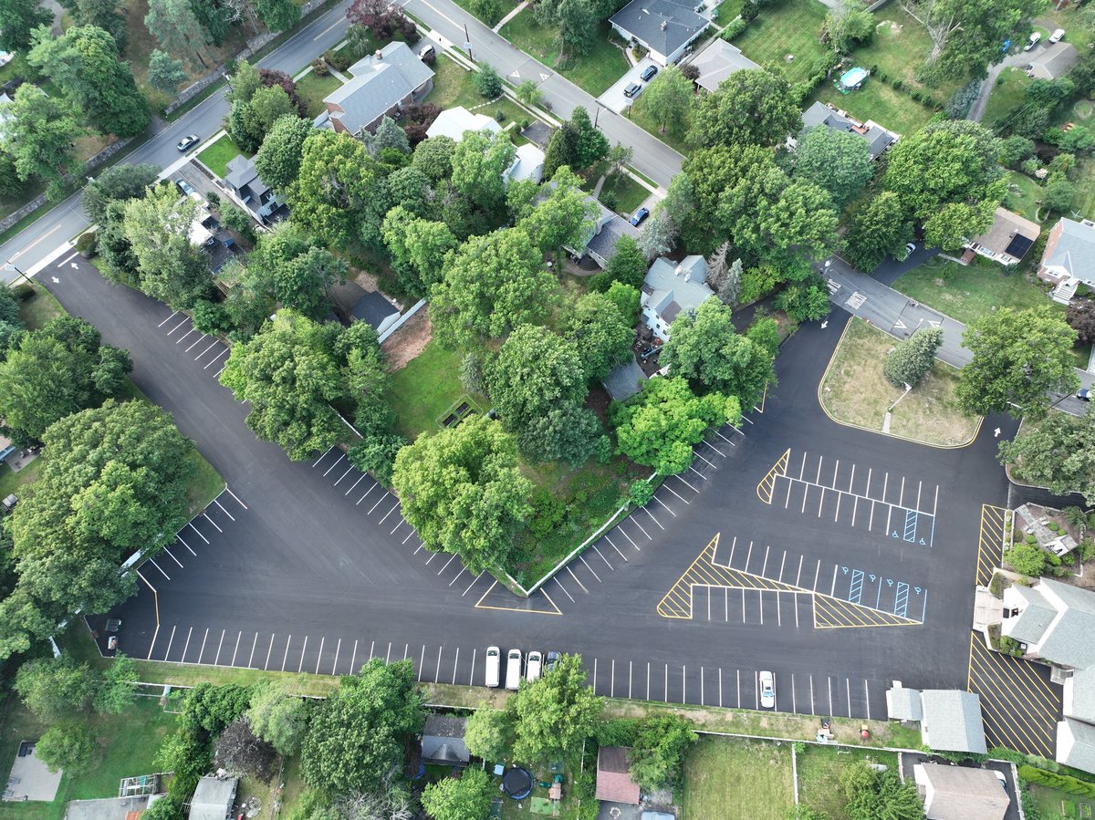 Overhead aerial of the full St. Joseph's parking lot after mill and pave, with fresh white, yellow, and blue striping.