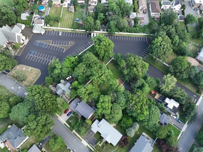Second overhead aerial of the St. Joseph's lot showing the paved drive aisles wrapping around the wooded parcel.