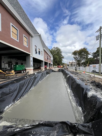 Sidewalk concrete pour along the red-brick and white-siding facade.