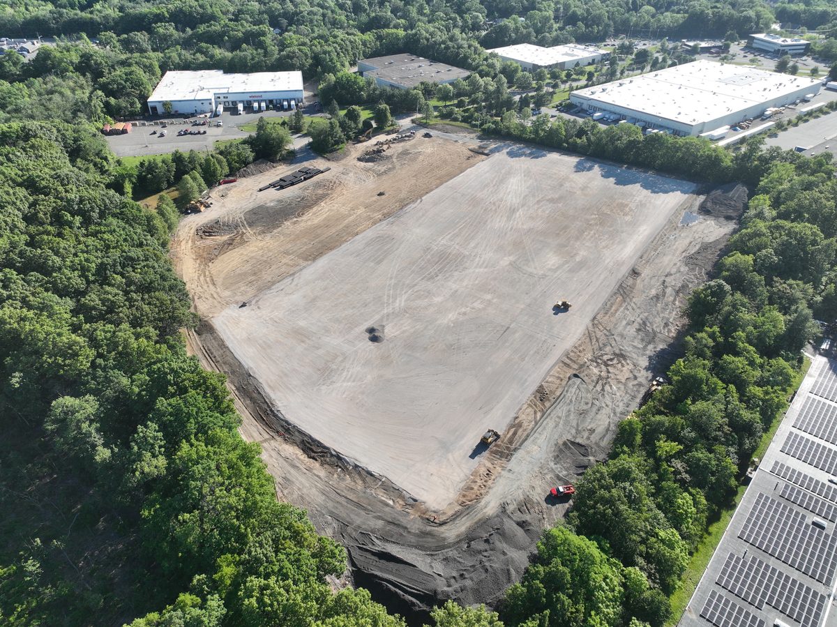 Angled aerial of the Parsippany warehouse pad — dozers grading, neighboring industrial buildings and solar arrays beyond.