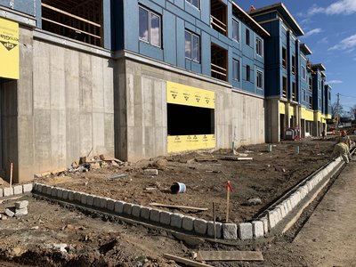 Long run of granite curbing newly installed along a freshly graded paving lift, building scaffolding visible in the background