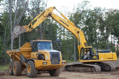 Komatsu PC400LC excavator loads soil into Deere articulated dump truck on cleared lot