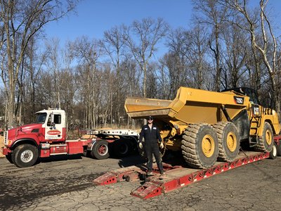 Operator stands beside Cat 725C articulated dump truck loaded onto a lowboy trailer