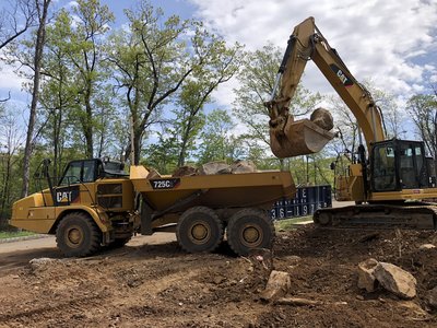 Cat excavator dumps boulder into Cat 725C articulated truck on excavation site
