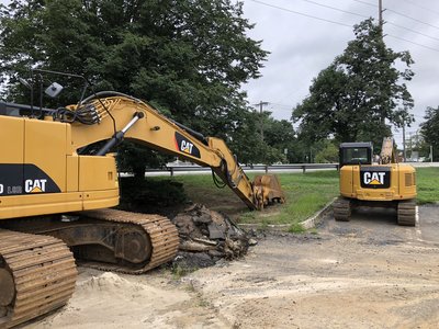 Two Cat excavators clearing stumps and debris on a commercial roadside lot