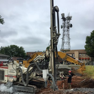 Terex foundation drill rig and excavator working beside a cell tower under overcast sky