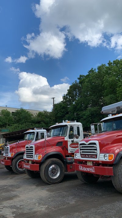 Row of red Mack dump trucks parked on a gravel lot under partly cloudy skies