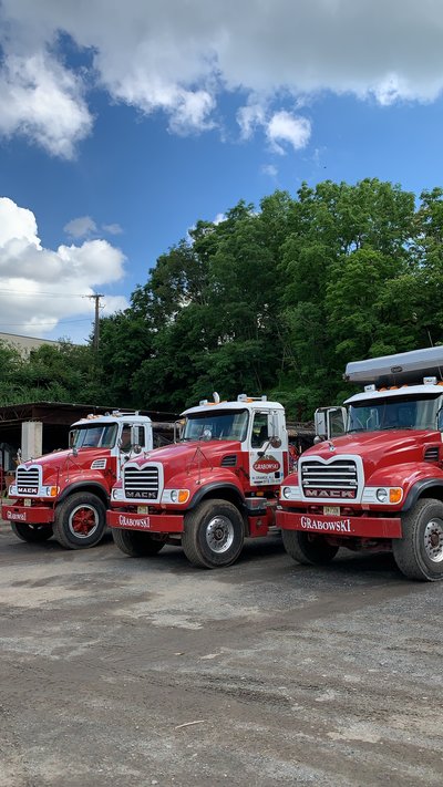 Three red Mack dump trucks lined up in a yard against a treeline