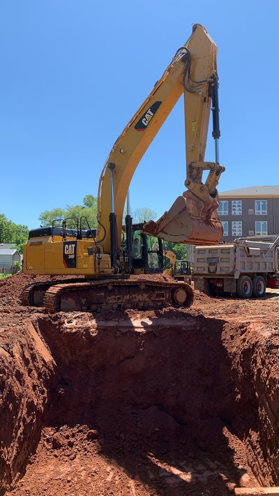 Cat excavator straddling an open foundation pit with a dump truck staged alongside
