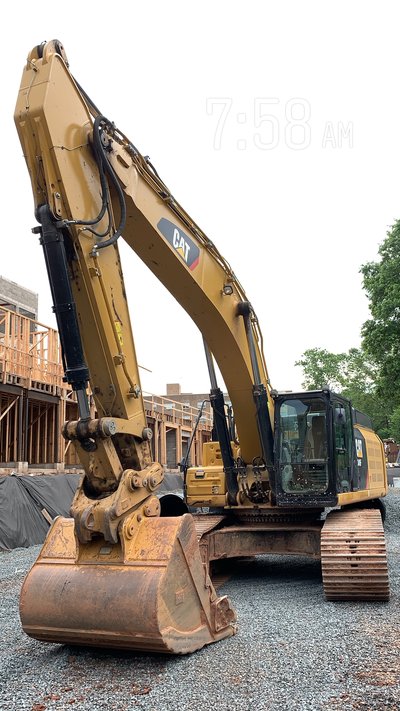 Cat excavator parked on gravel near framed multistory structures in early morning light