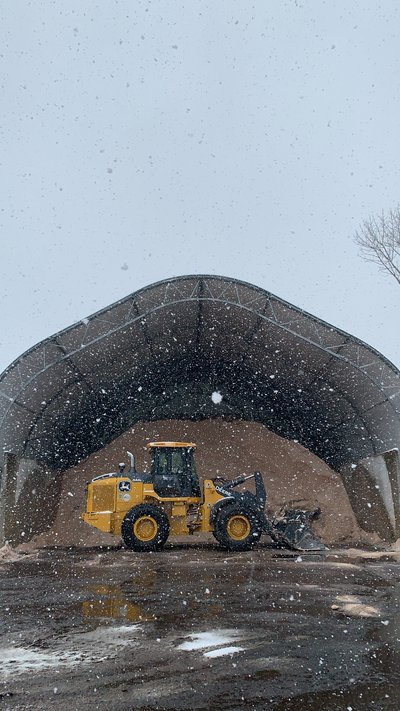 Deere wheel loader pushing material under a fabric storage shelter during light snowfall
