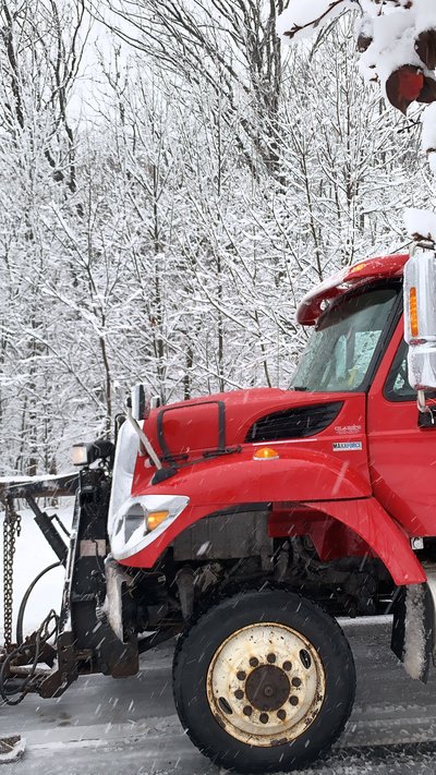 Red plow truck parked among snow-covered trees during a winter storm