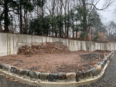 Cleared lot bounded by concrete retaining walls and stone curbing along a wooded edge