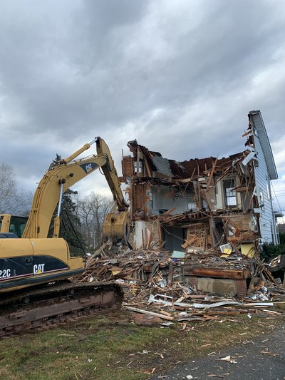 Cat 322C excavator demolishing a two-story wood-framed house under overcast sky