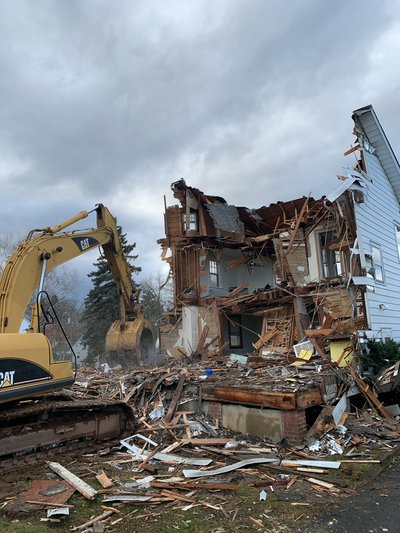 Cat excavator tearing into the upper floor of a residential structure with debris piling below
