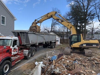 Cat 322C excavator loading demolition debris into a Mack dump trailer on a residential lot