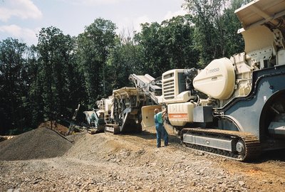 Worker beside a Metso mobile crusher processing rock into aggregate at a wooded site