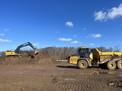 Deere excavator and articulated dump truck working a graded earthwork site under blue sky