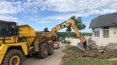 Cat excavator and Komatsu HM300 articulated truck excavating beside a residential building