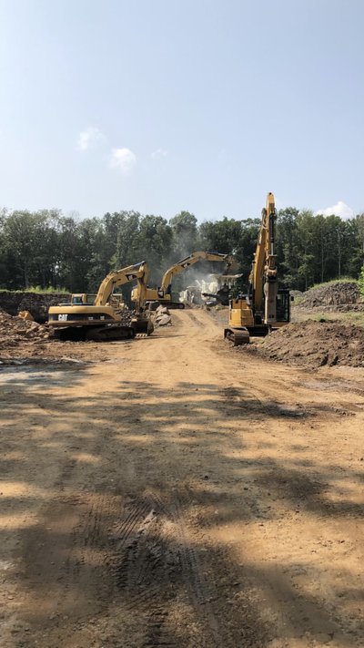 Three Cat excavators work alongside crushing operation on a wooded earthwork site