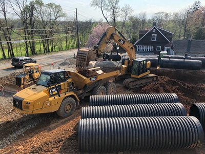 CAT articulated dump truck and excavator install large HDPE detention pipes on roadside