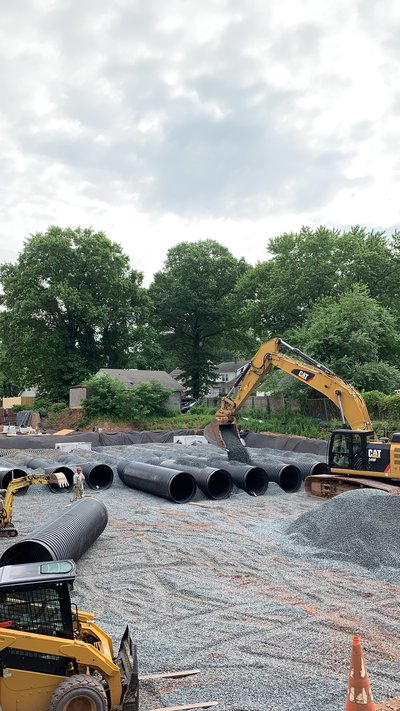 Excavator placing large HDPE detention pipes onto gravel bedding with skid steer nearby