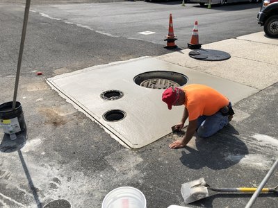 Worker finishes fresh concrete pad around new manhole and drain inserts in parking lot
