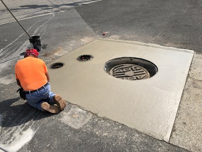 Worker hand-finishes wet concrete pad around manhole frame and drain openings on pavement