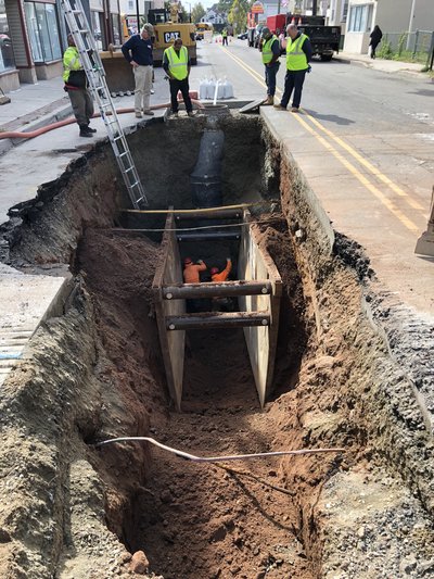 Worker inside trench box at deep road cut with new pipe and ladder access