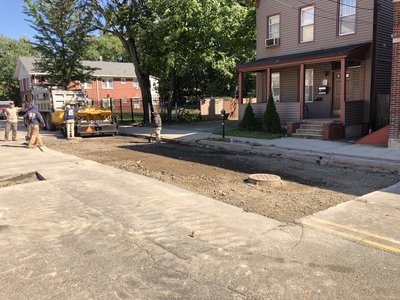 Restored dirt patch with manhole cover beside curb after utility work near residential homes