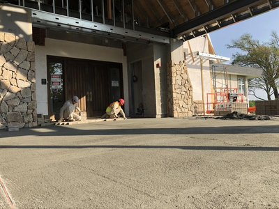 Two masons set stone veneer at building entrance with freshly screeded concrete pad nearby