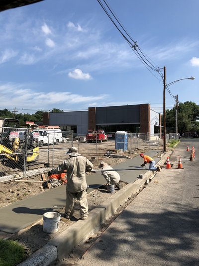 Crew screeds and finishes long concrete sidewalk pour beside curb on sunny day