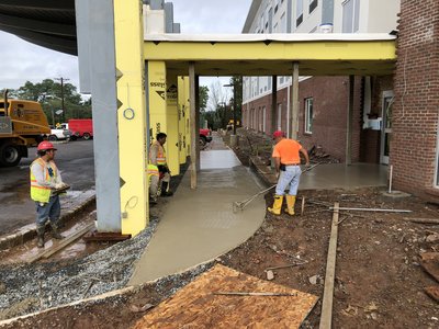 Workers finish wet concrete walkway under canopy roof at multistory building entrance