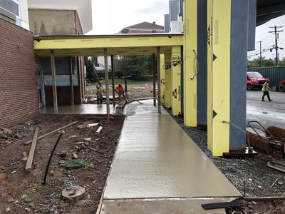 Freshly poured concrete walkway curves under steel canopy frame at building site entrance