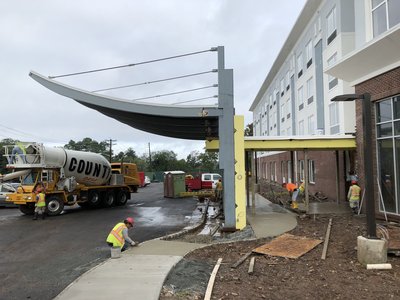 Concrete mixer truck delivers material as crew finishes curved walkway beside multistory building