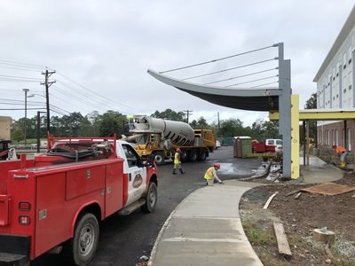 Service truck and concrete mixer parked near workers finishing curved sidewalk under canopy