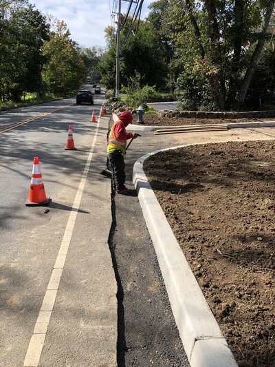 Worker installs granite curbing along roadside with traffic cones diverting passing vehicles