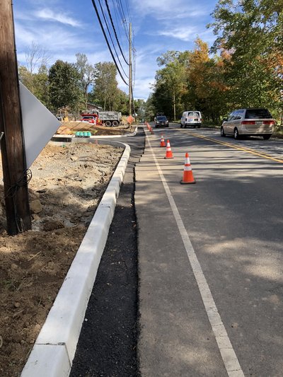 Newly set granite curbing lines roadway edge with fresh asphalt strip and traffic cones