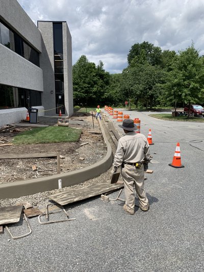 Worker finishes a curved granite-faced curb beside a sidewalk near an office building